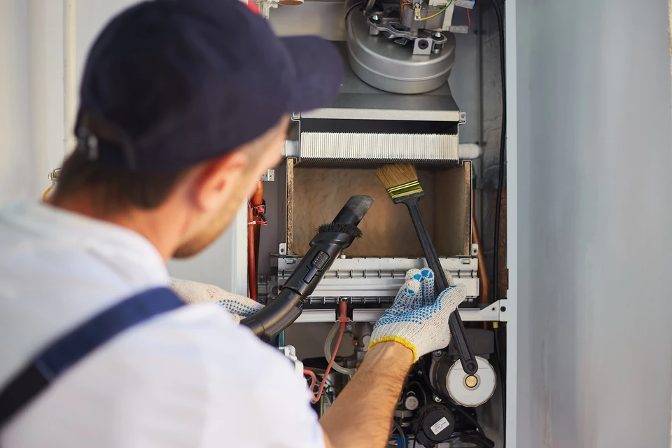Un technicien en uniforme effectue la maintenance d'une chaudière à gaz domestique