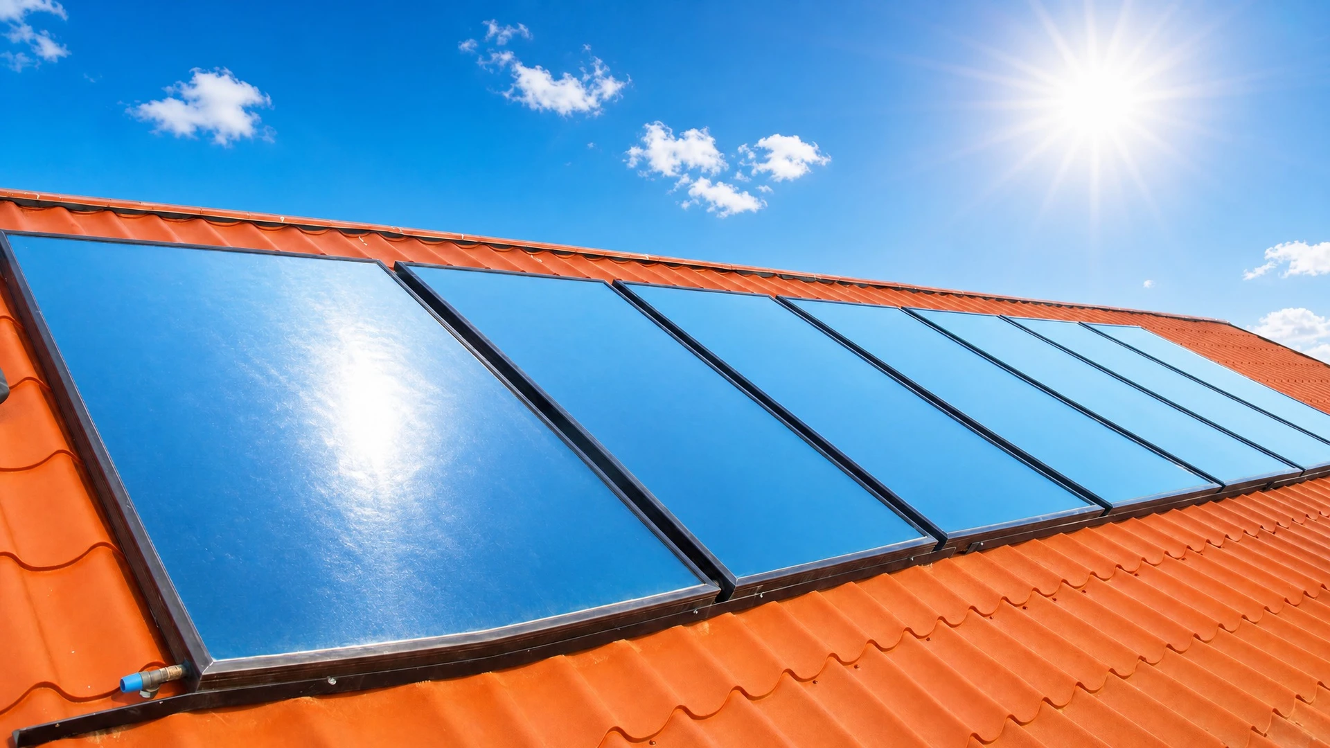 Panneaux solaires thermiques à capteurs plans installés en rangée sur une toiture en tuiles métalliques rouge